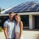 Ein glückliches Paar steht lächelnd in der Einfahrt eines großen Hauses mit installierten Sonnenkollektoren.