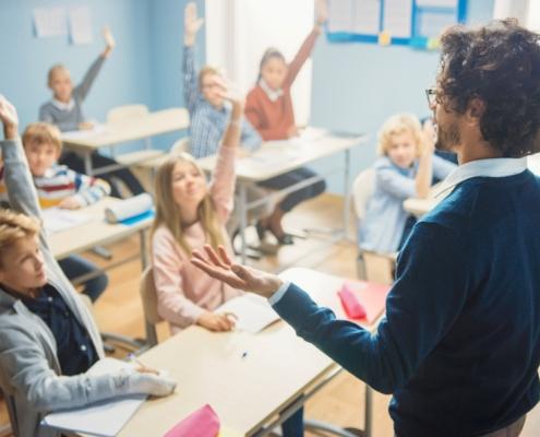 Lehrer mit lockigem Haar interagiert mit diversen Schülern im Klassenzimmer eines privaten Gymnasiums in Berlin, fördert aktive Teilnahme und Engagement.