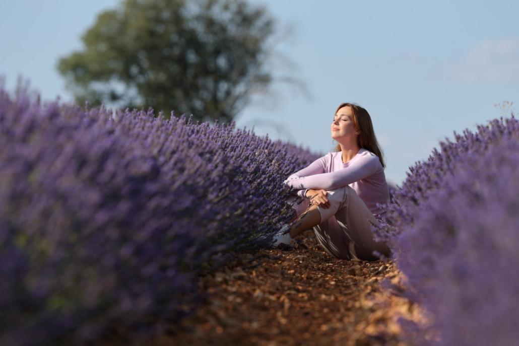 Frau sitzt entspannt in einem Lavendelfeld und genießt die Natur, während sie ein Einweg Vape verwendet. Das Bild vermittelt Ruhe, Gelassenheit und die Verbindung von modernen Entspannungstechniken mit der Natur.