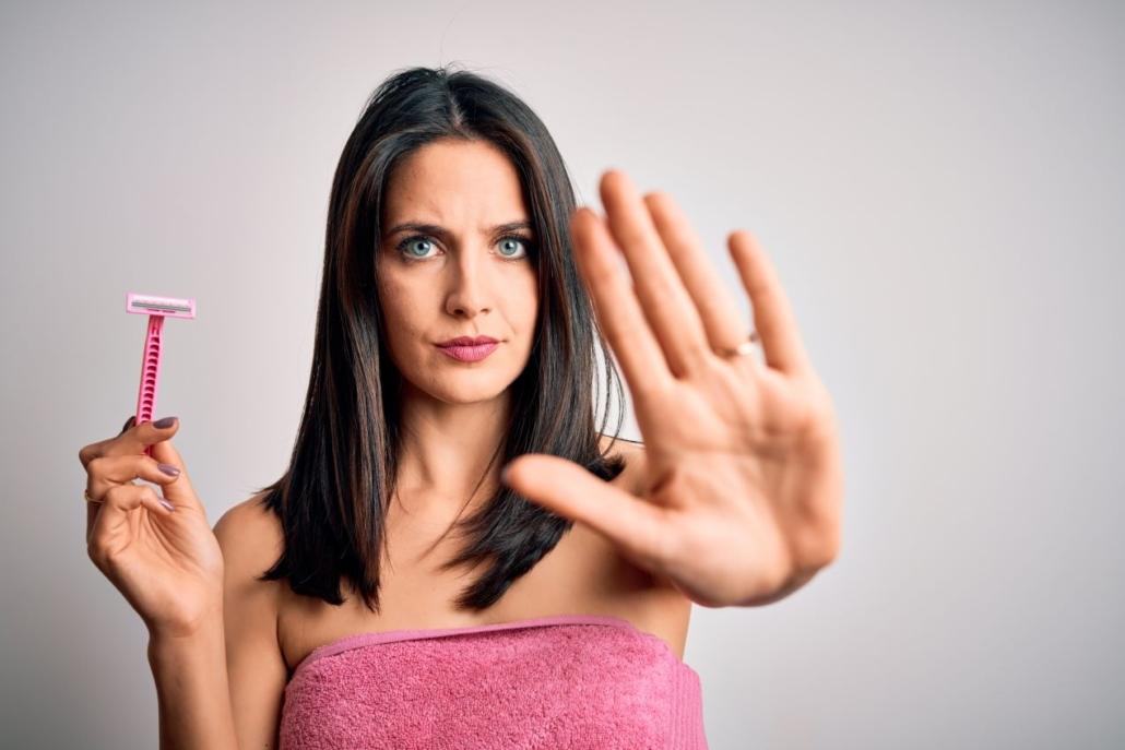 Frau in rosa Handtuch hält Einwegrasierer und zeigt mit Handfläche „Stopp“ – nachhaltiger Rasierer Damen als Alternative