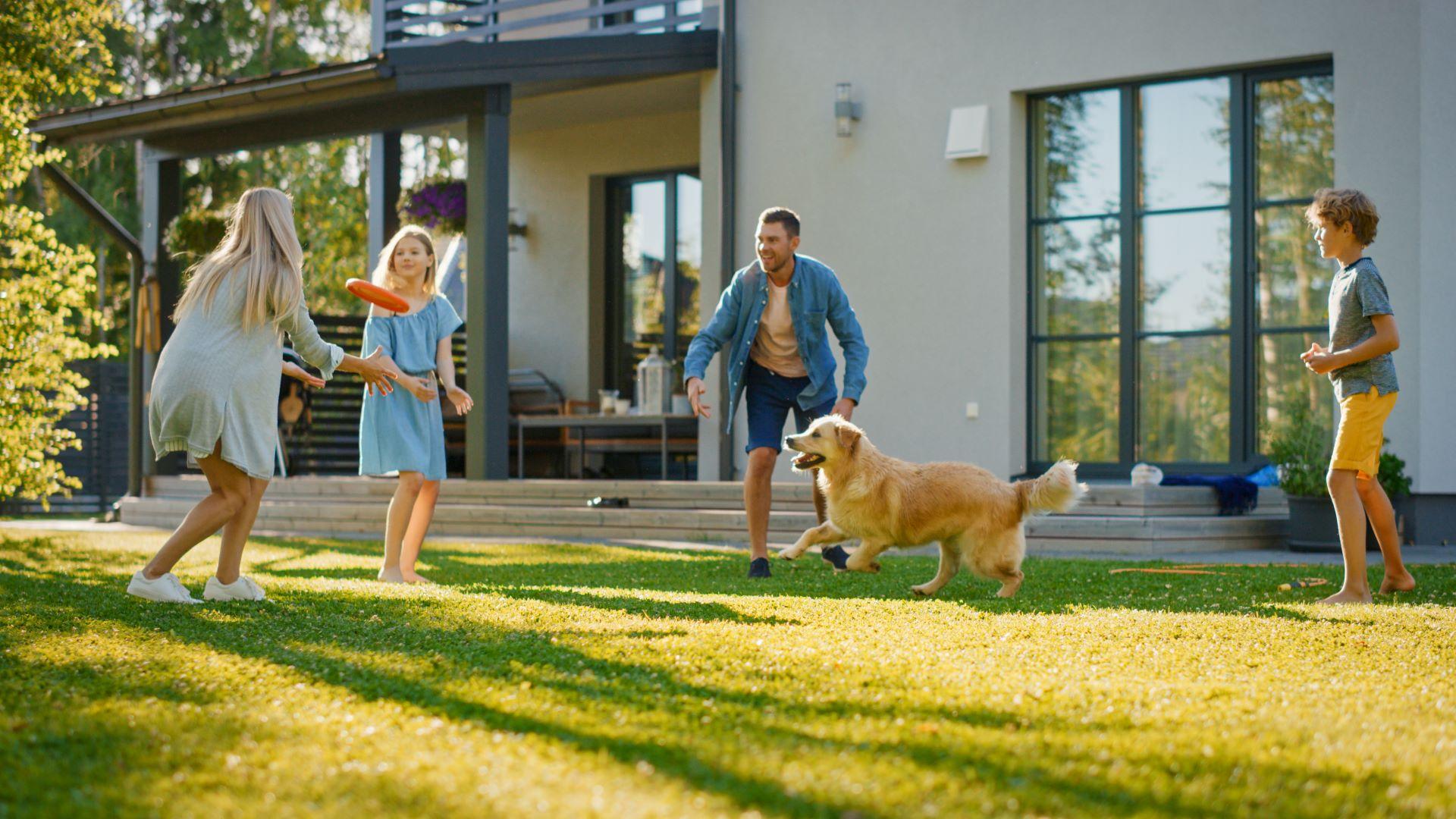 Familie spielt im Garten mit Hund, geschützt durch Überdachung mit Doppelstegplatten 10 mm am Haus.