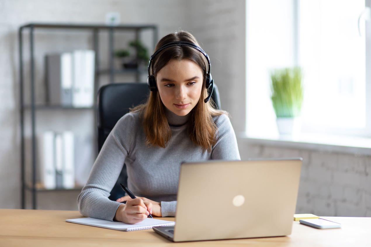 Eine Frau mit Headset am Laptop, während sie digitale Inhalte durch einen E-Learning Anbieter nutzt, um ihre Fähigkeiten flexibel weiterzuentwickeln.