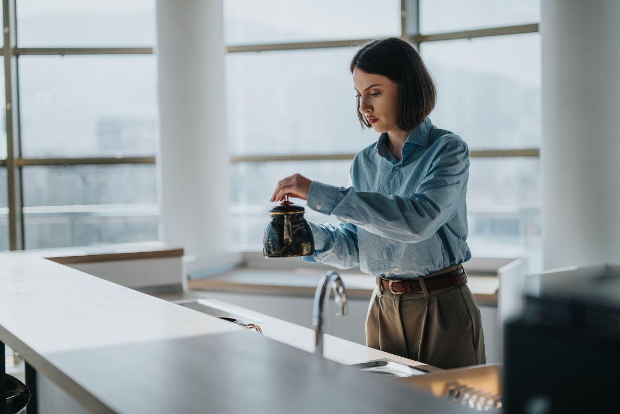 Frau in einer modernen Büroküche in Berlin bereitet Tee zu – Sauberkeit und Hygiene im Büroalltag.