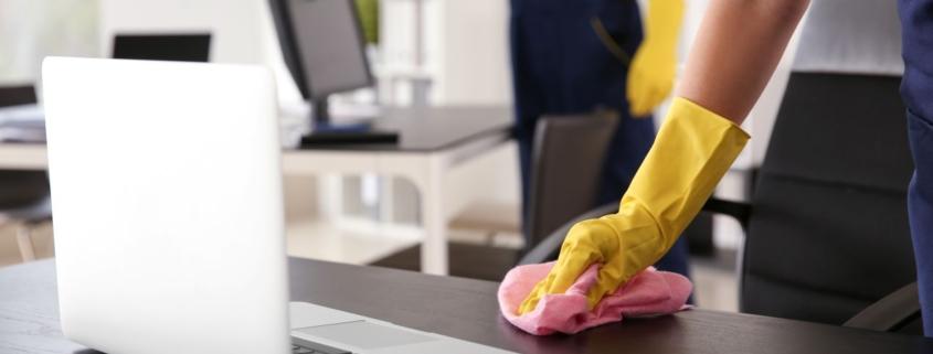 Professionelle Büroreinigung in Berlin – Reinigungskraft mit gelben Handschuhen wischt einen Schreibtisch für mehr Hygiene im Büro.