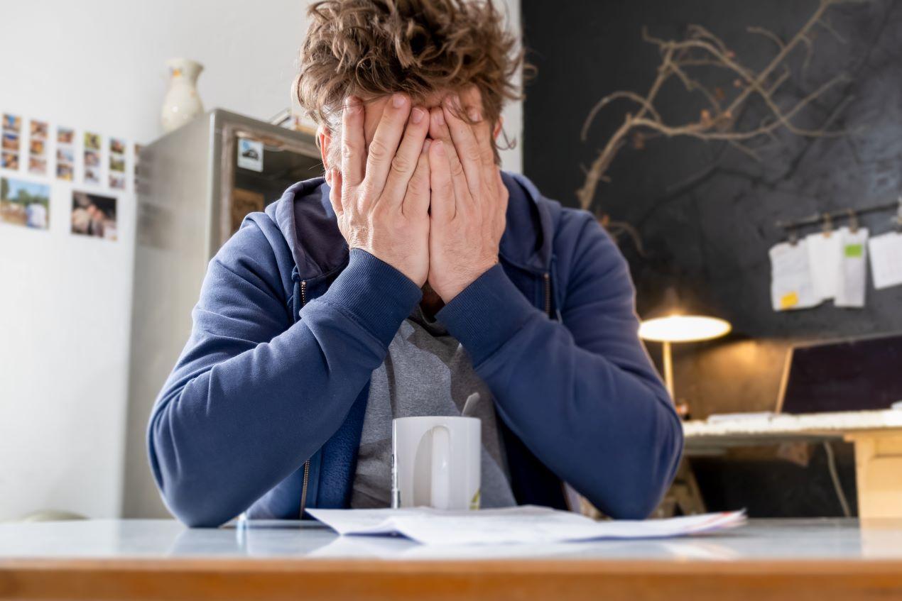 Ein Mann sitzt verzweifelt am Tisch mit einem Kündigungsschreiben – emotionale Auswirkungen und Stress als mögliche Gründe für eine kündigungsschutzklage.