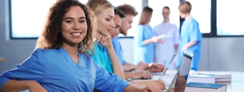 Junge Pflegeauszubildende in blauer Berufskleidung arbeiten gemeinsam am Laptop – moderner Unterricht in der Ausbildung Pflegehelfer