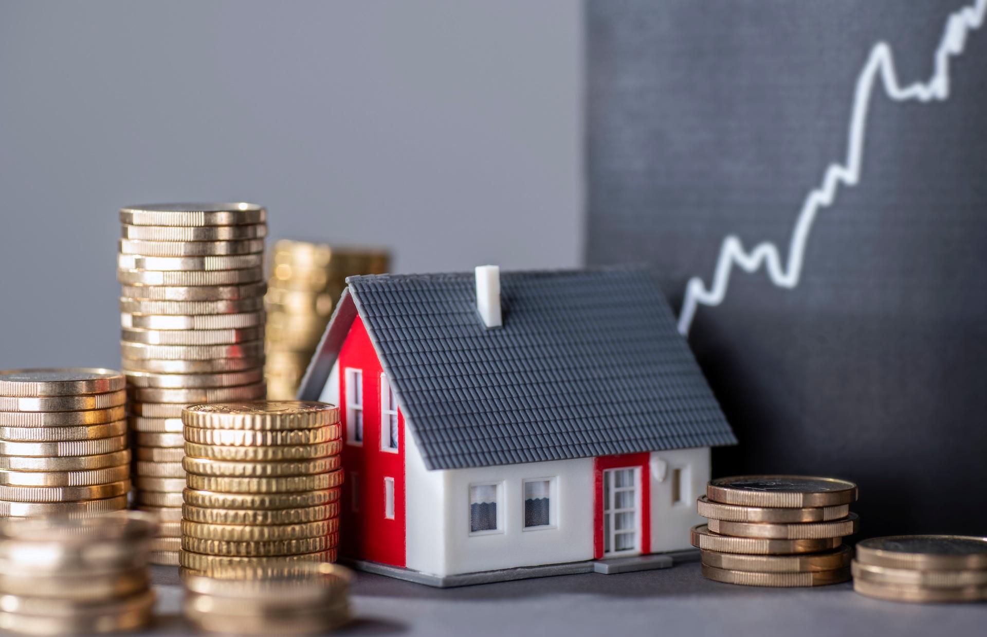 Hausmodell zwischen Geldstapeln vor Wachstumskurve | Immobilienfinanzierung Krefeld

