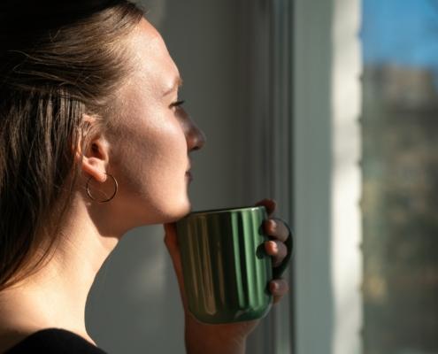 Nachdenkliche Frau mit Tasse am Fenster | Elfliq Liquid