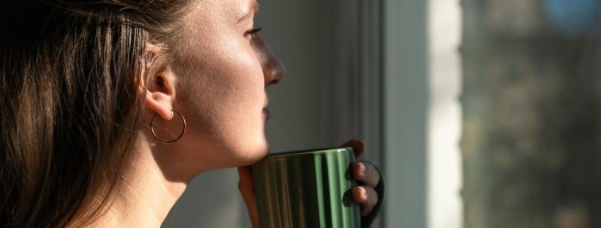 Nachdenkliche Frau mit Tasse am Fenster | Elfliq Liquid