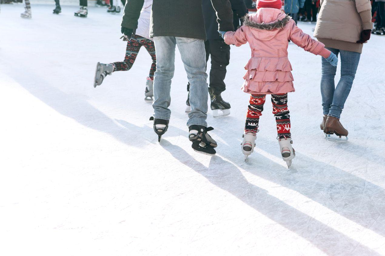 Schlittschuhe an den Füßen einer Familie beim Eislaufen, Kind mit pinker Jacke und bunter Leggings