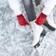 Schlittschuhe werden auf einer Eisfläche geschnürt, rote Winterhandschuhe halten die Schnürung fest