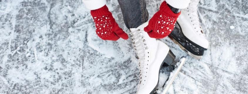 Schlittschuhe werden auf einer Eisfläche geschnürt, rote Winterhandschuhe halten die Schnürung fest