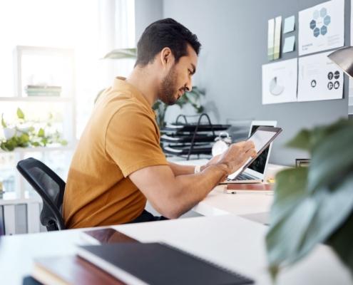 Mann arbeitet im Buero mit Tablet an Content-Planung, Erklaervideo als Teil der Landingpage-Strategie sichtbar im Hintergrund