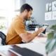 Mann arbeitet im Buero mit Tablet an Content-Planung, Erklaervideo als Teil der Landingpage-Strategie sichtbar im Hintergrund