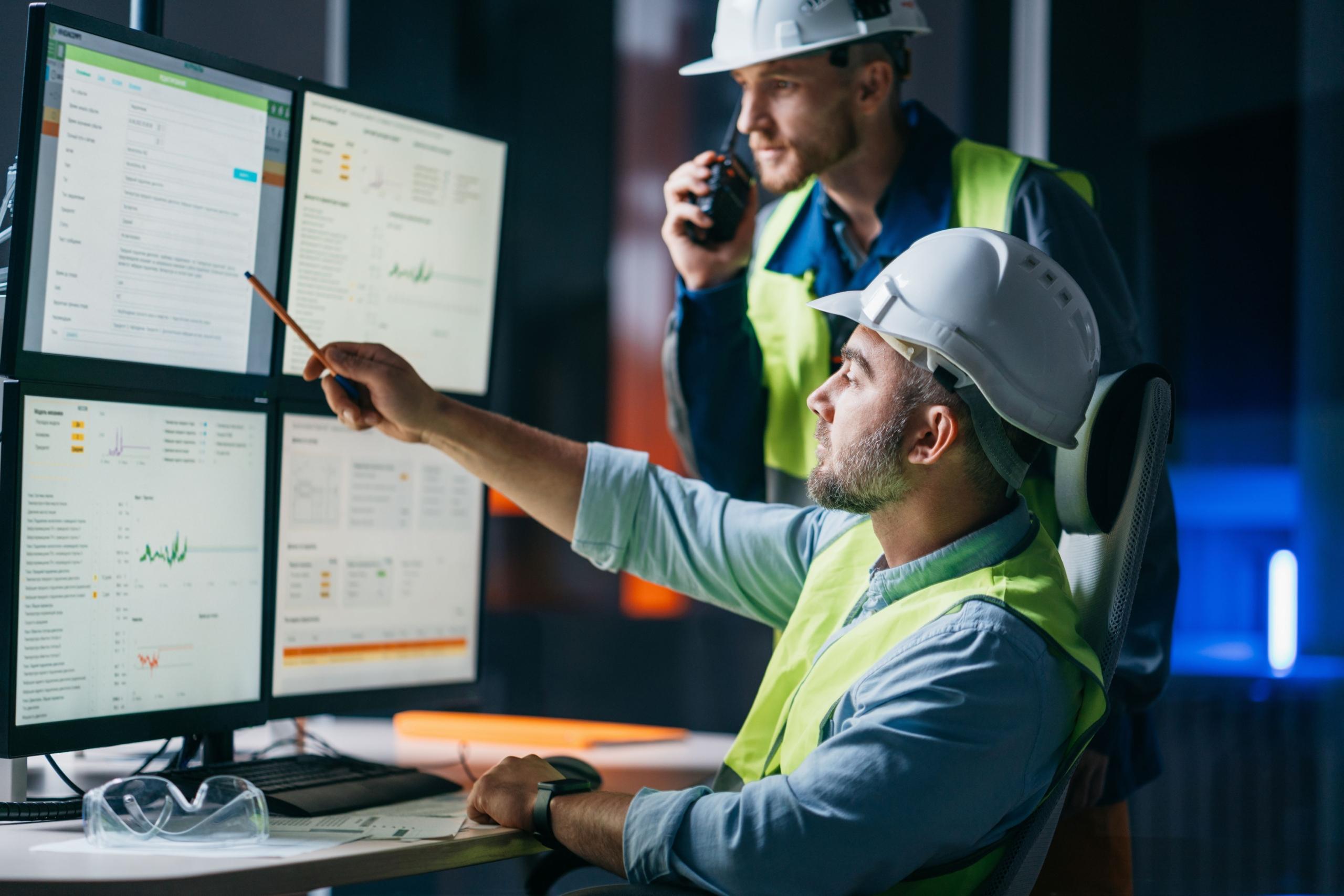 Zwei Mitarbeiter analysieren Produktionsdaten mit Produktionsplanung Software an mehreren Monitoren