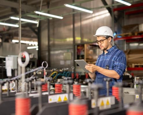 Mitarbeiter mit Helm nutzt Produktionsplanung Software auf Tablet in moderner Fertigungshalle