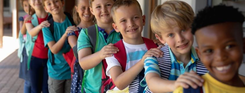 Reihe lachender Schüler mit Rucksäcken im Schulflur | Grundschule Berlin